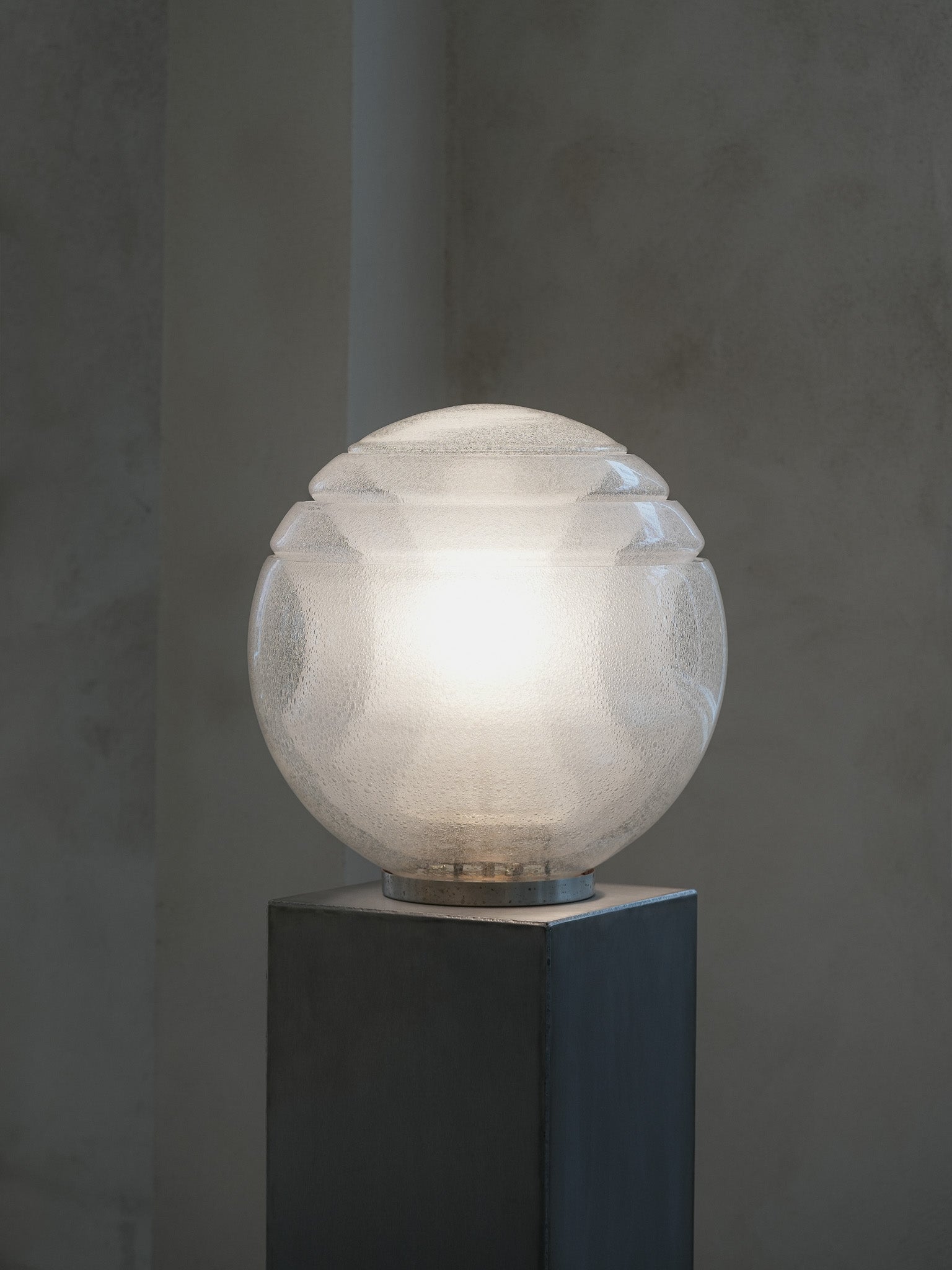 Vintage LT328 table lamp, designed by Carlo Nason for Mazzega in the 1970s. Featuring a circular metal base, this lamp is composed of four stacked glass elements that form a large, luminous globe. The air bubbles within the glass add a sense of lightness and an ethereal quality, beautifully diffusing the central light source. Available at RUE VERTE