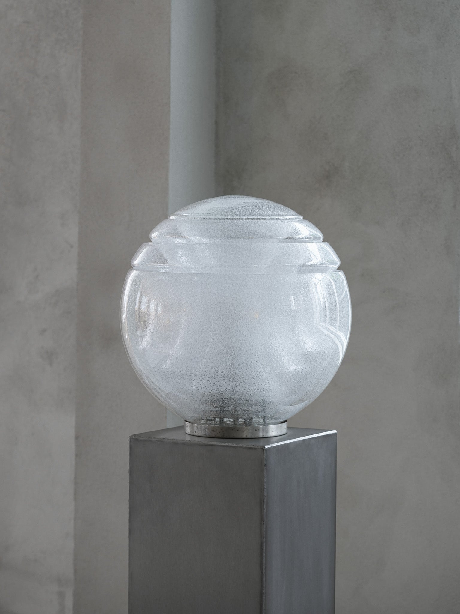 Vintage LT328 table lamp, designed by Carlo Nason for Mazzega in the 1970s. Featuring a circular metal base, this lamp is composed of four stacked glass elements that form a large, luminous globe. The air bubbles within the glass add a sense of lightness and an ethereal quality, beautifully diffusing the central light source. Available at RUE VERTE